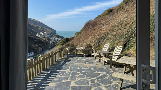 A stone pathway leading to a wooden deck with chairs and benches overlooking a coastal village.