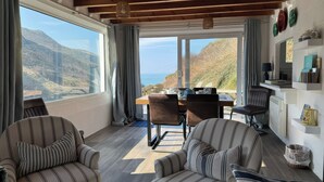 A cozy room with a dining area, two striped armchairs, a wooden ceiling, and a view of the mountains.