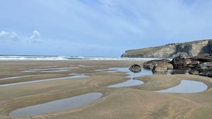 A coastal landscape with a sandy beach, rocky outcrops, and a cliff.
