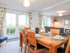A dining area with a wooden table set for four, surrounded by chairs. There is a sofa and a lamp in the background. - Arnside House (Carnforth)