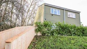 Eine Holzterrasse führt zu einem Haus mit grüner Fassade und einem kleinen Fenster.