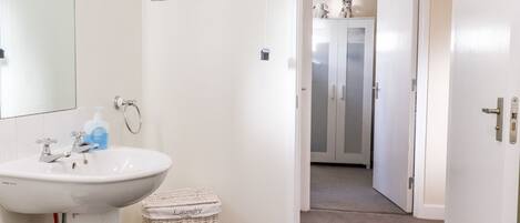 Un baño con un lavabo blanco, un espejo, una botella de jabón y una cesta de mimbre para la ropa.