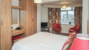 Une chambre d’hôtel avec un lit, un bureau et une chaise, une télévision et deux chaises rouges.