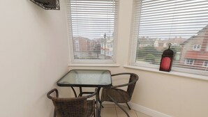 Une pièce d’angle avec une petite table et deux chaises, une fenêtre avec des stores et une lanterne rouge posée sur le rebord.