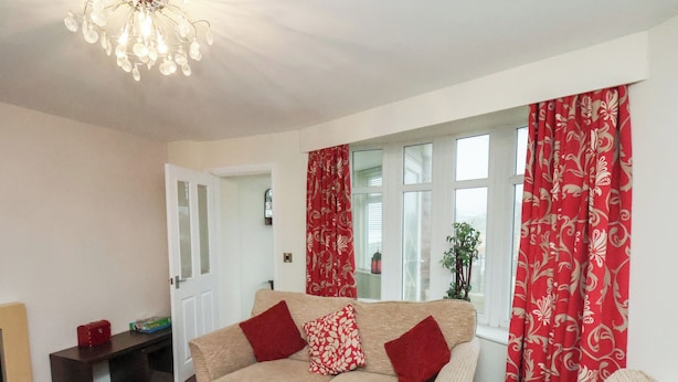 Un salon avec un canapé beige, des coussins à motifs rouges et blancs, un tapis rouge et un lustre.