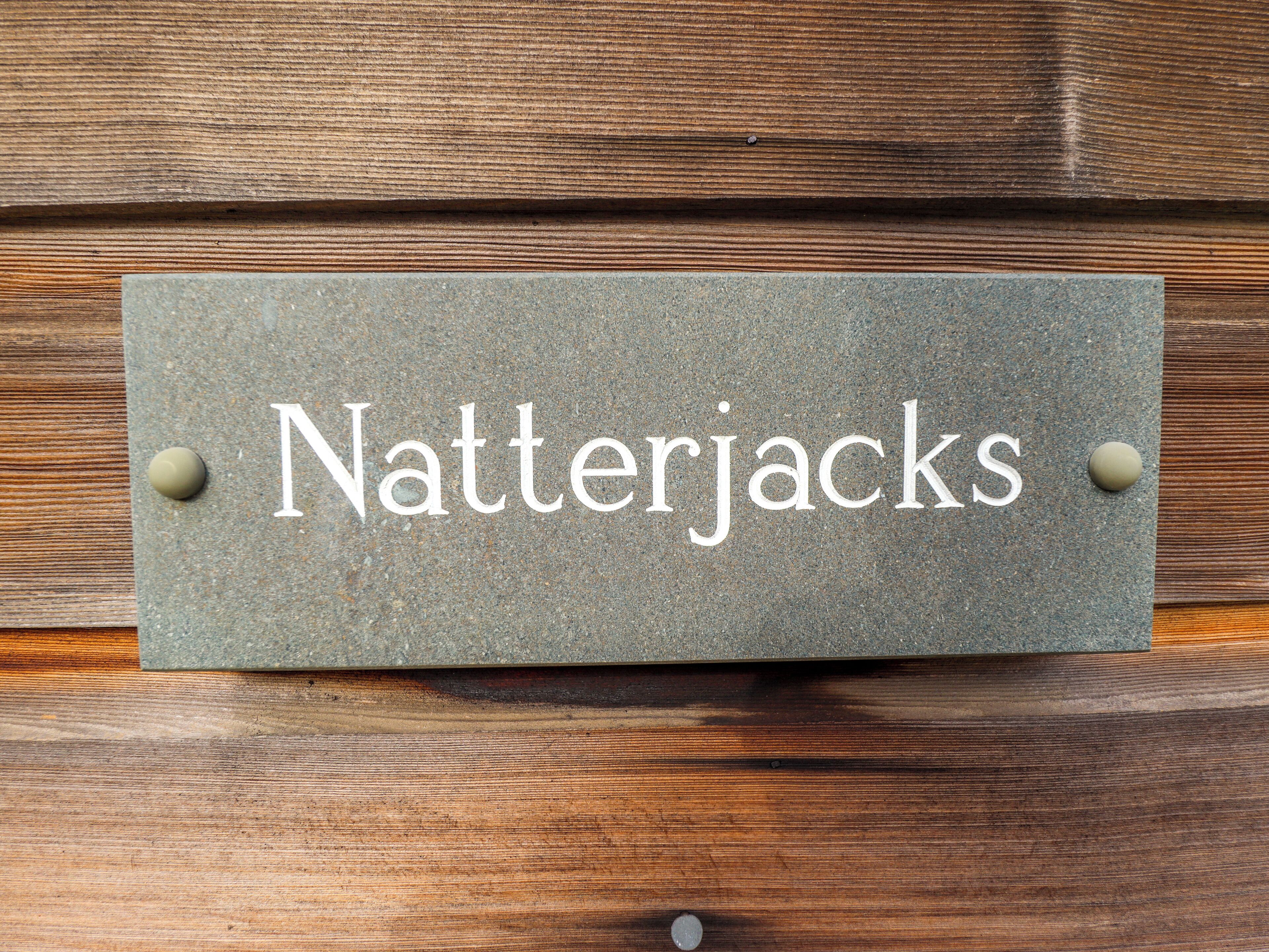 A rectangular sign with the text "Natterjacks" mounted on a wooden surface with two round pegs.