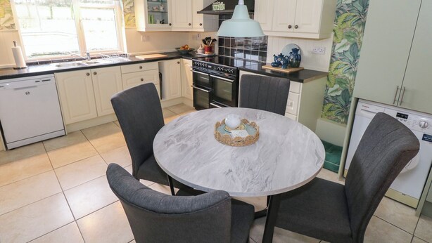 A kitchen with white cabinets, a round marble table, and grey chairs. - Kivvy Cottage (Carrigallen)