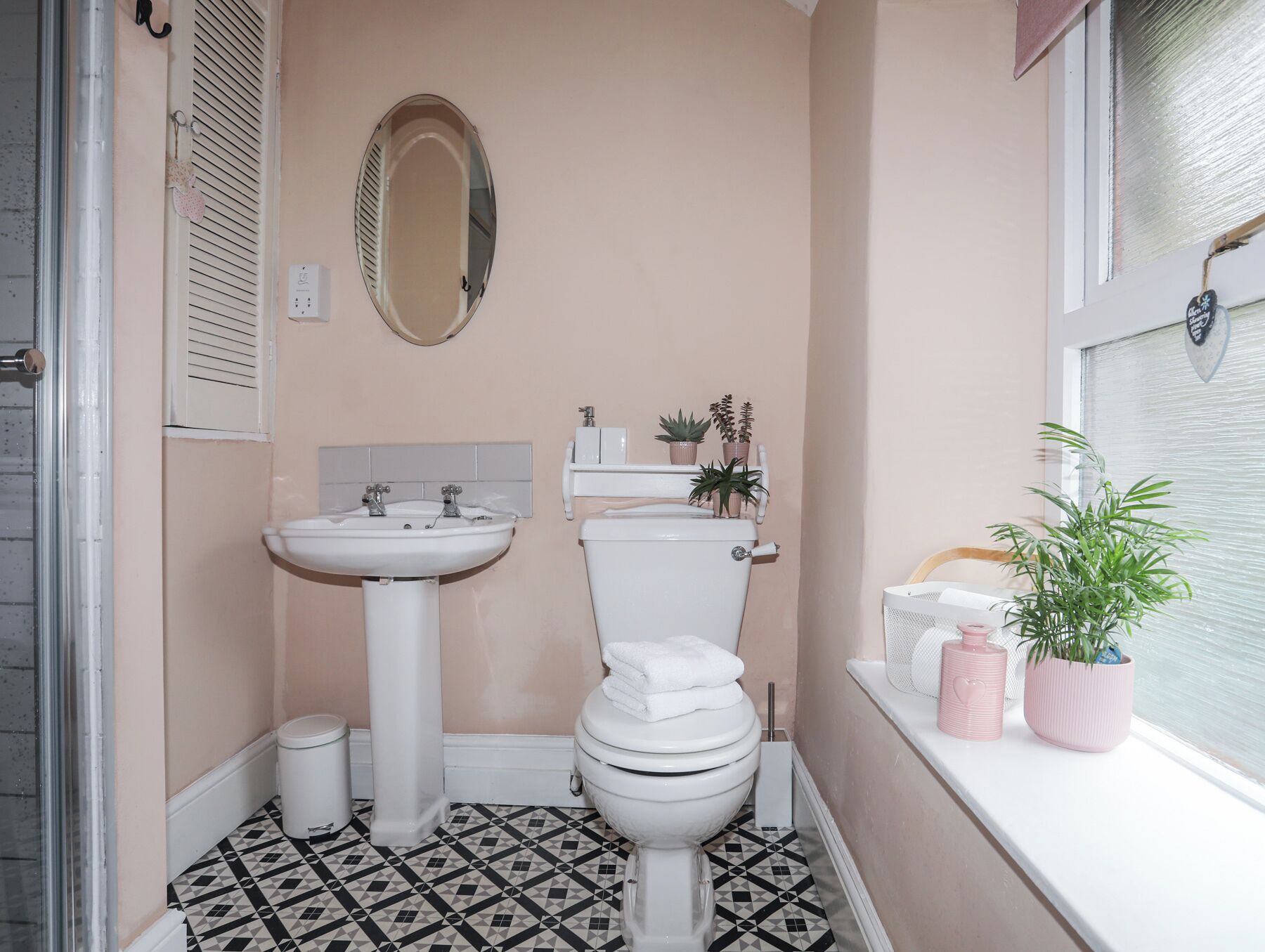 Une salle de bain avec un lavabo, des toilettes et une fenêtre agrémentée de plantes.