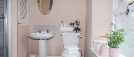 Une salle de bain avec un lavabo, des toilettes et une fenêtre agrémentée de plantes.