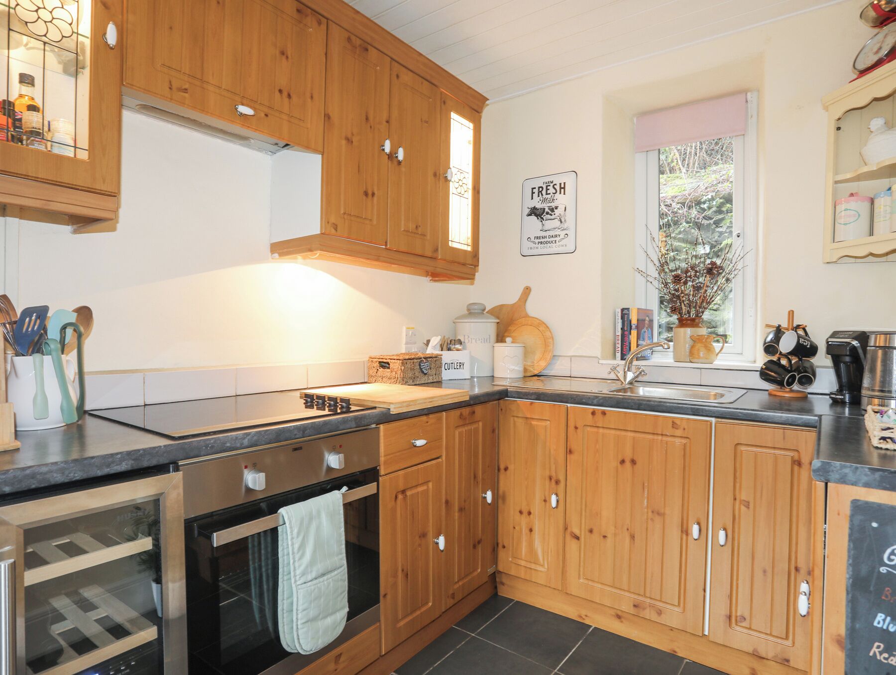 A kitchen with wooden cabinets, a stove, a sink, and a window with a view of trees.