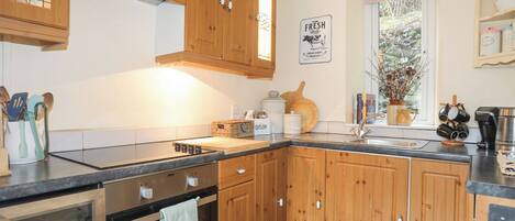 A kitchen with wooden cabinets, a stove, a sink, and a window with a view of trees.