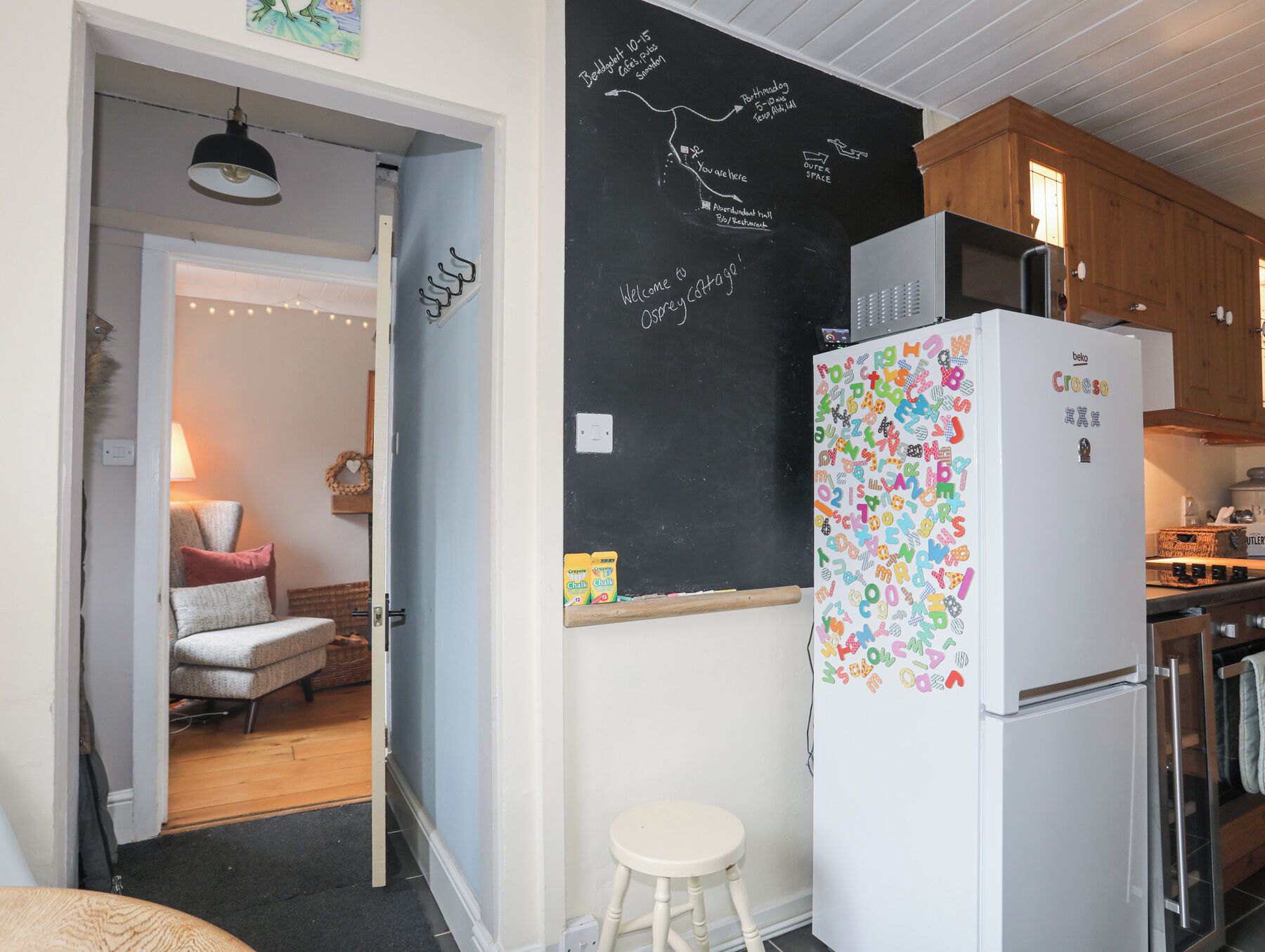 A kitchen with a chalkboard, a refrigerator, and a dining area with a chair and a table.