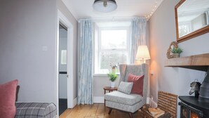 Ein gemütliches Wohnzimmer mit Kamin, einer Couch, einem Sessel und einem fenster mit Vorhängen.