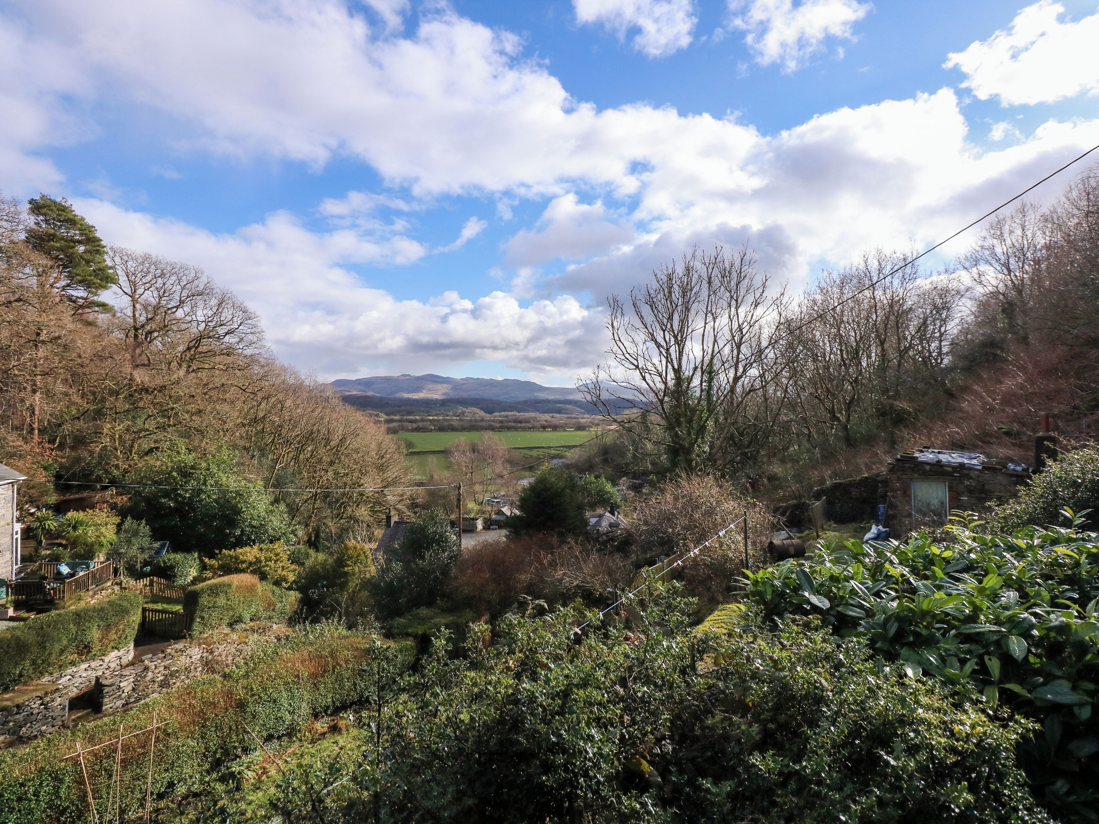 A rural landscape with a stone house, a stone wall, and a small garden.