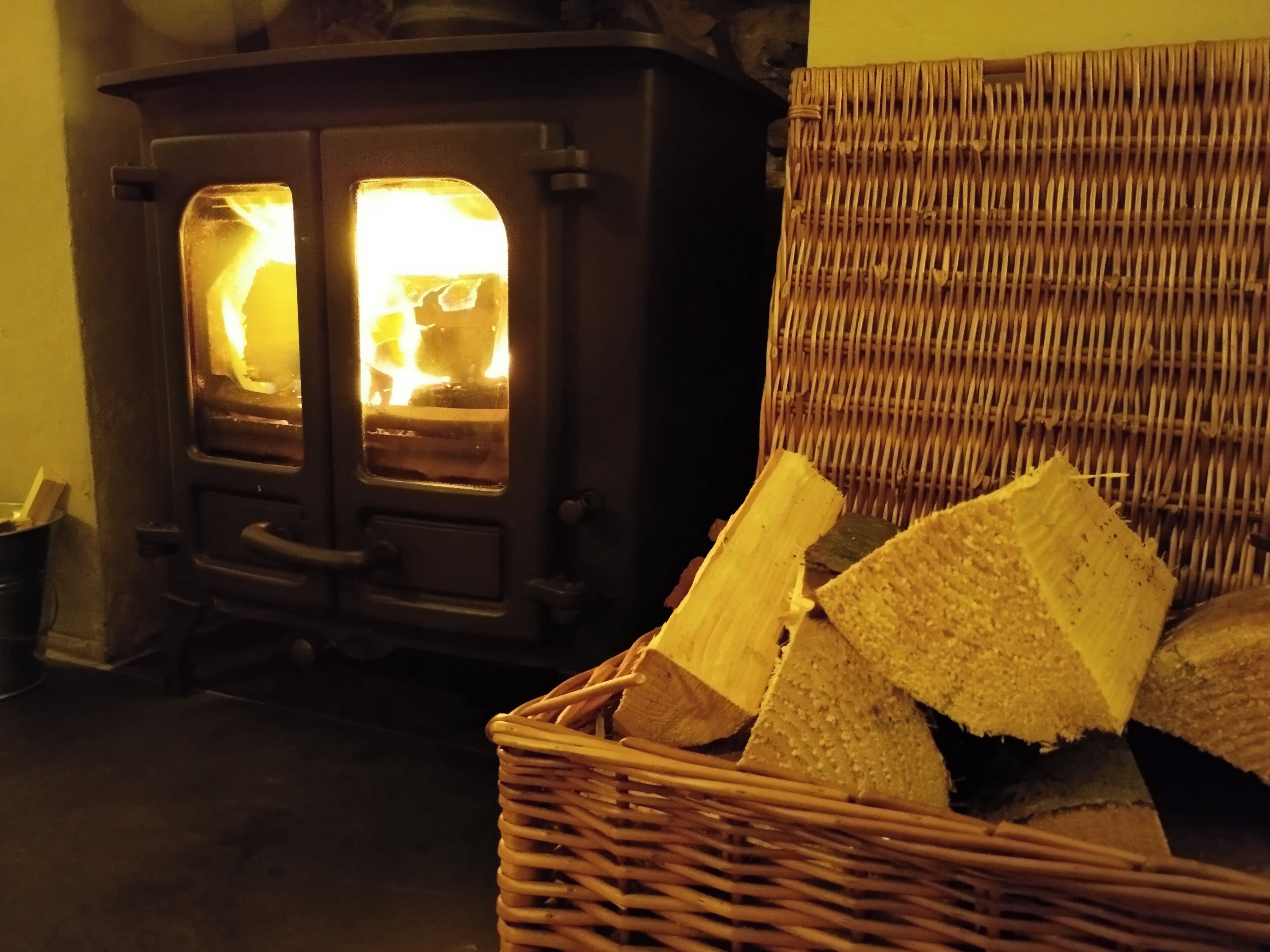 A room with a wood-burning stove and a wicker basket filled with firewood.