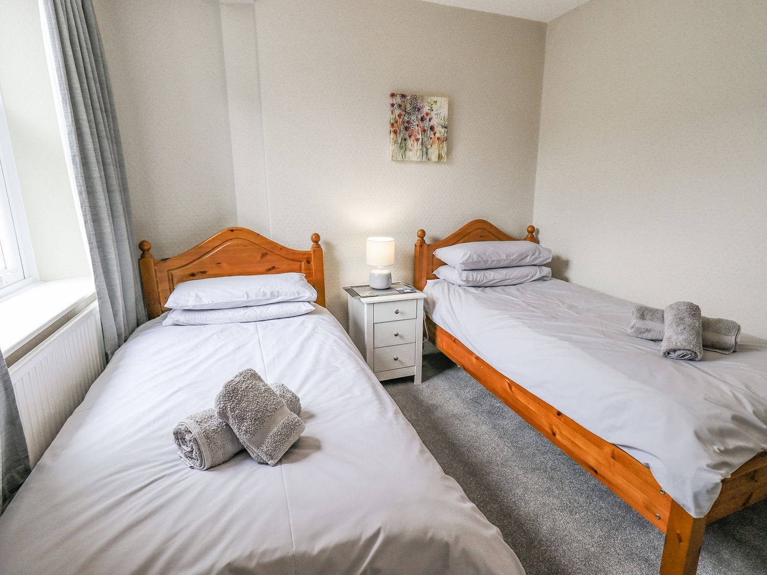 A hotel room with two single beds, a bedside table with a lamp, and a painting on the wall.