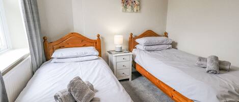 A hotel room with two single beds, a bedside table with a lamp, and a painting on the wall.