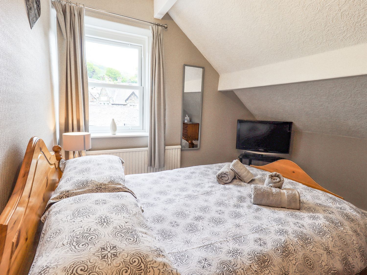 A bedroom with a bed, a TV, and a window with curtains.