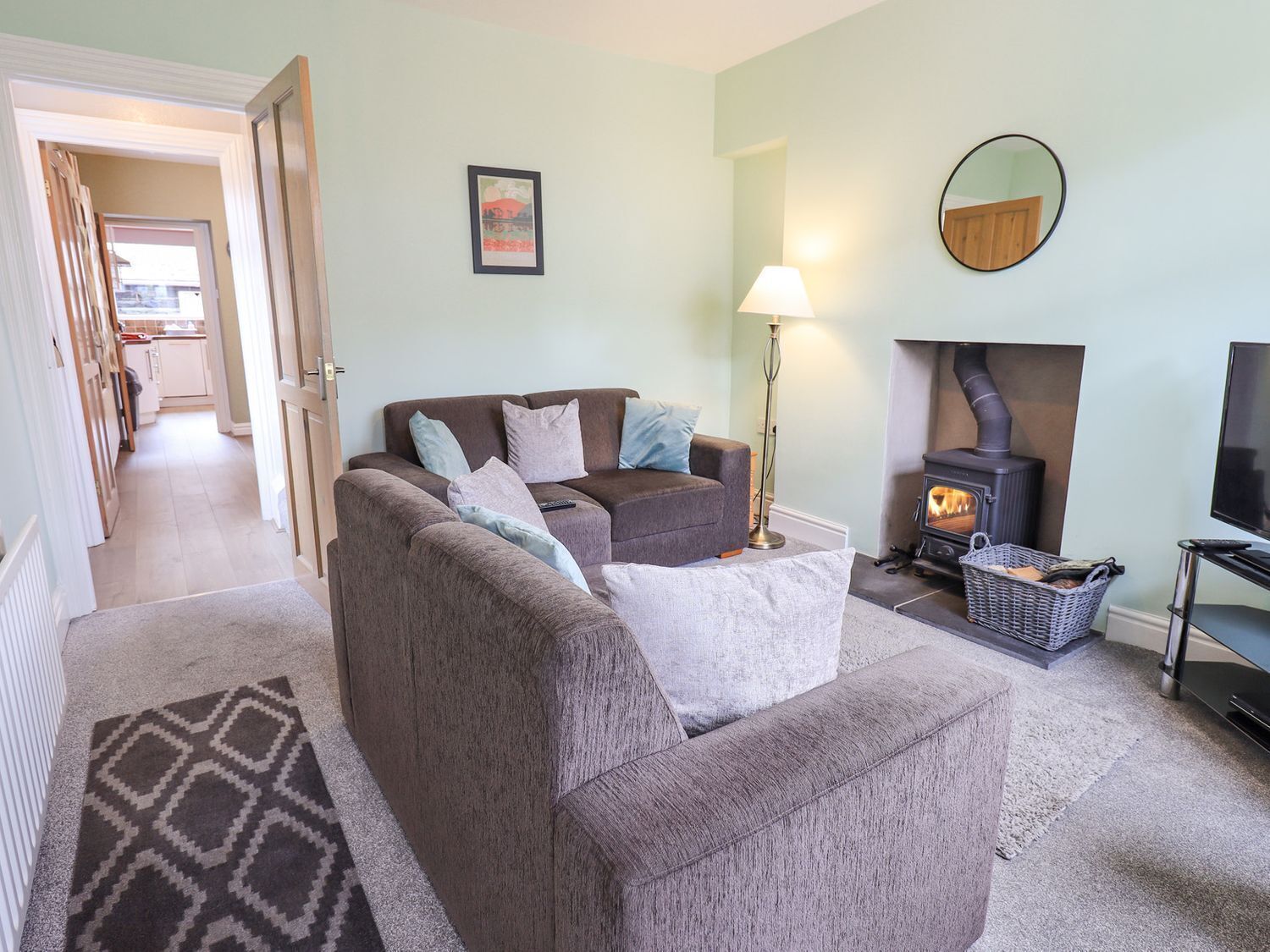 A living room with a sofa set, a fireplace, a television, and a hallway leading to a kitchen.