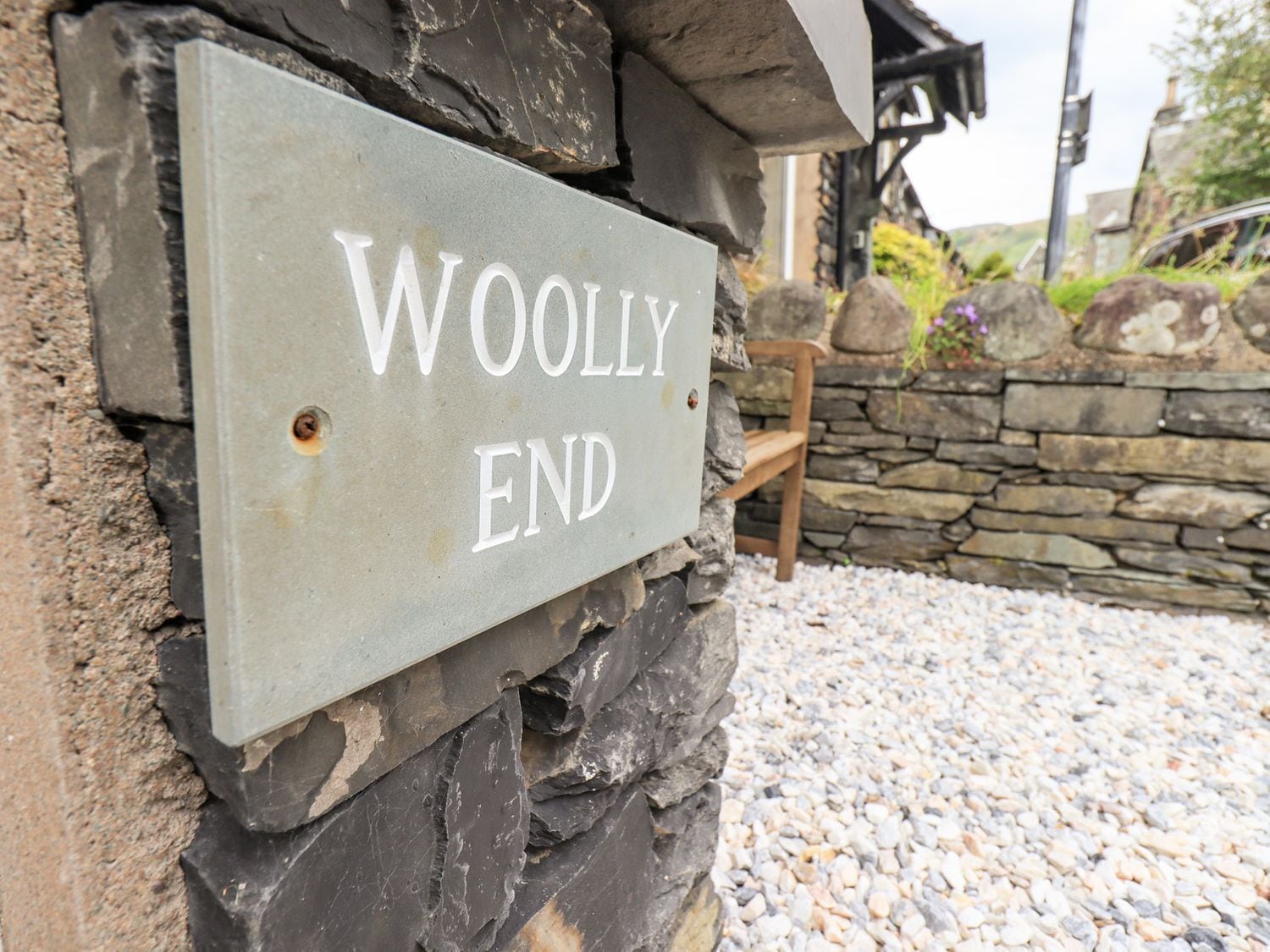 A sign reading "WOOLLY END" mounted on a stone wall.