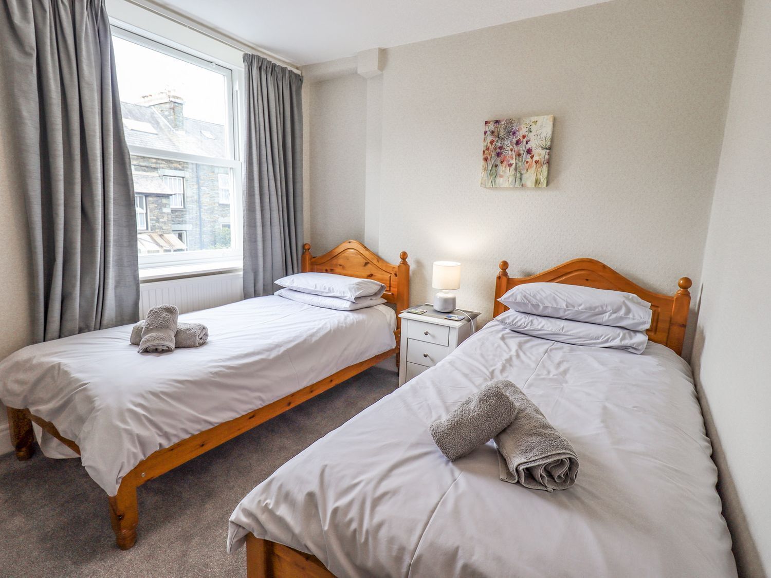 Une chambre double avec deux lits, une fenêtre avec des rideaux, une table de chevet avec une lampe et un tableau au mur.