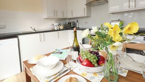 Et moderne køkken med hvide skabe, en sort bordplade og et spisebord dækket med tallerkener, en skål med frugt, en vinflaske og en vase med blomster.