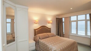 Een hotelkamer met een groot bed, twee wandlampen, een raam met gordijnen en een kledingkast met spiegel.