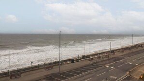 Een kustweg met een strand aan de rechterkant, met een rij bankjes en een hek langs de boulevard.
