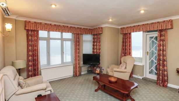 Een woonkamer met een bank, fauteuil en salontafel. Er is een televisie en een raam met gordijnen.