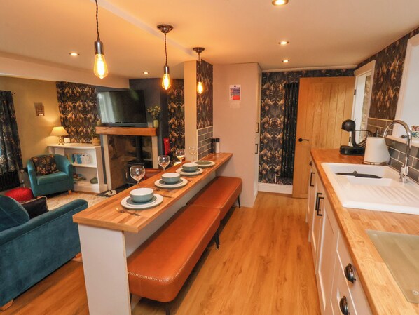 A modern kitchen with a wooden countertop, bench seating, and a built-in oven. - Seascape Cottage (Redcar)