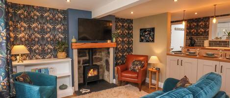 A cozy living room with a fireplace, a television, and a kitchen area.