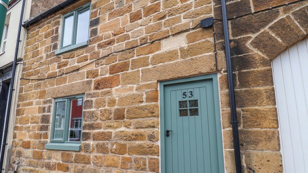 Un bâtiment en pierre avec une porte verte portant le numéro 53, une fenêtre et un petit jardinier avec des fleurs.
