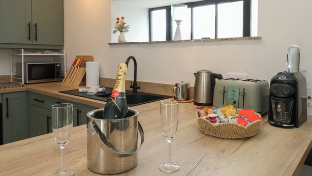 Une cuisine moderne équipée d’un four à micro-ondes, d’un grille-pain, d’une bouilloire et d’une machine à café. On peut voir une bouteille de champagne dans un seau en métal, ainsi que deux verres posés sur le comptoir.