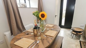 Une table à manger dressée avec des couverts, une bouteille de champagne et un vase rempli de fleurs.