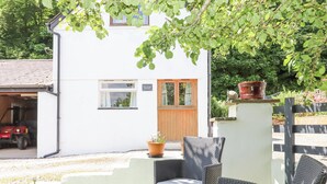 Un edificio blanco con puerta de madera, un garaje y un patio con mobiliario de mimbre y una planta en maceta.