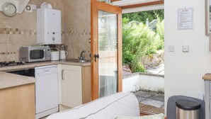 Cocina compacta con microondas, estufa y lavavajillas, un lavamanos pequeño y una puerta que da a un jardín.