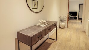 Un pasillo moderno con una consola de madera, una obra de arte enmarcada y un florero con ramas.