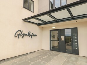 Entrada de un edificio con toldo de vidrio, una placa con el nombre "Glynnifon" y una puerta con panel de control.