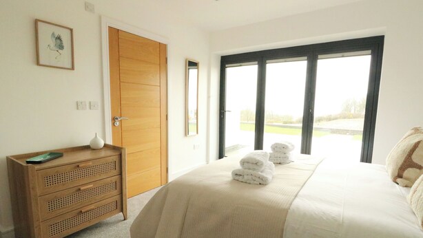 Een slaapkamer met een bed, een houten dressoir, een lijst met een afbeelding en een groot raam met uitzicht.