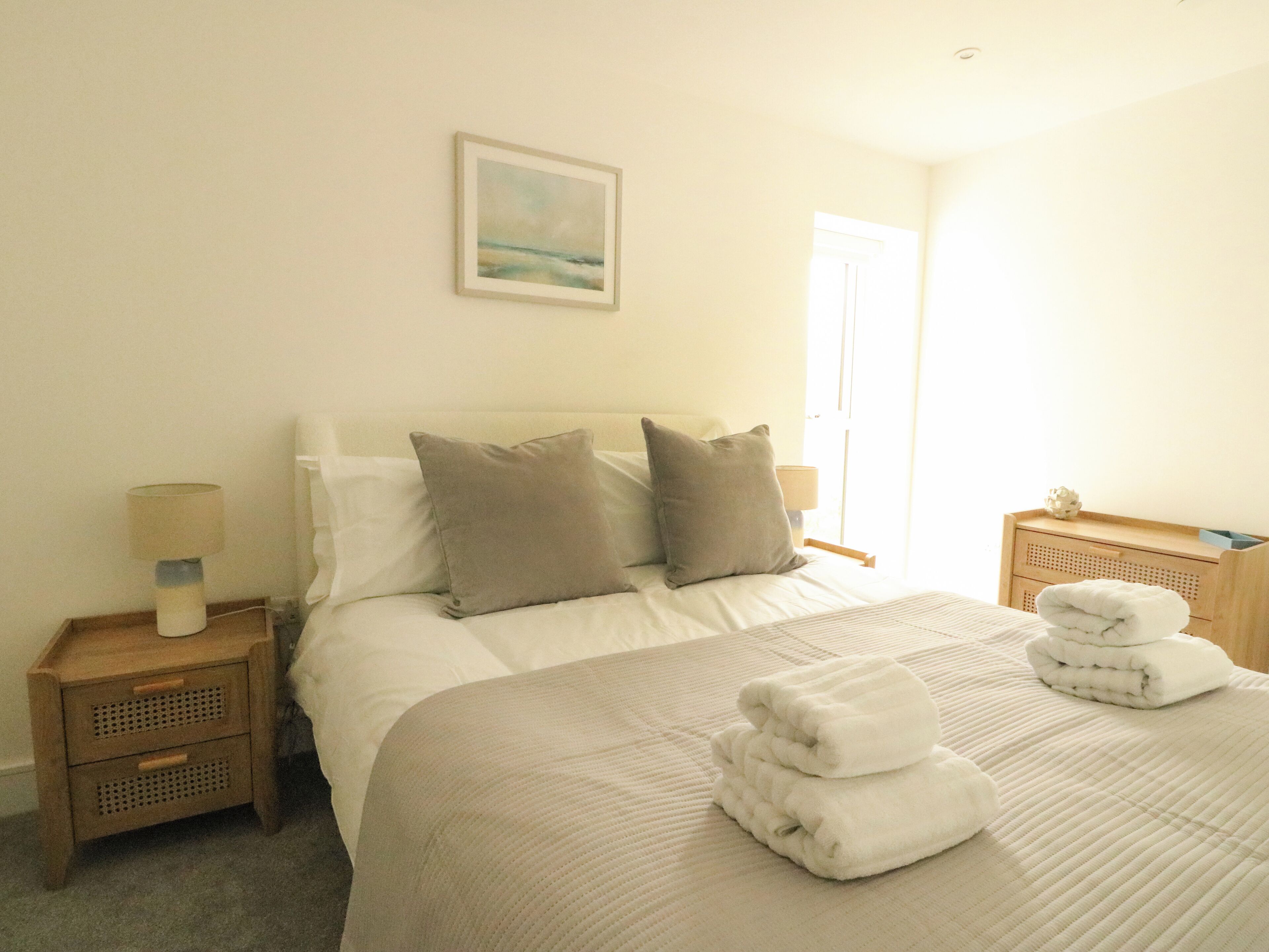 A neatly made bed with pillows, a bedside lamp, and a folded towel on the nightstand.