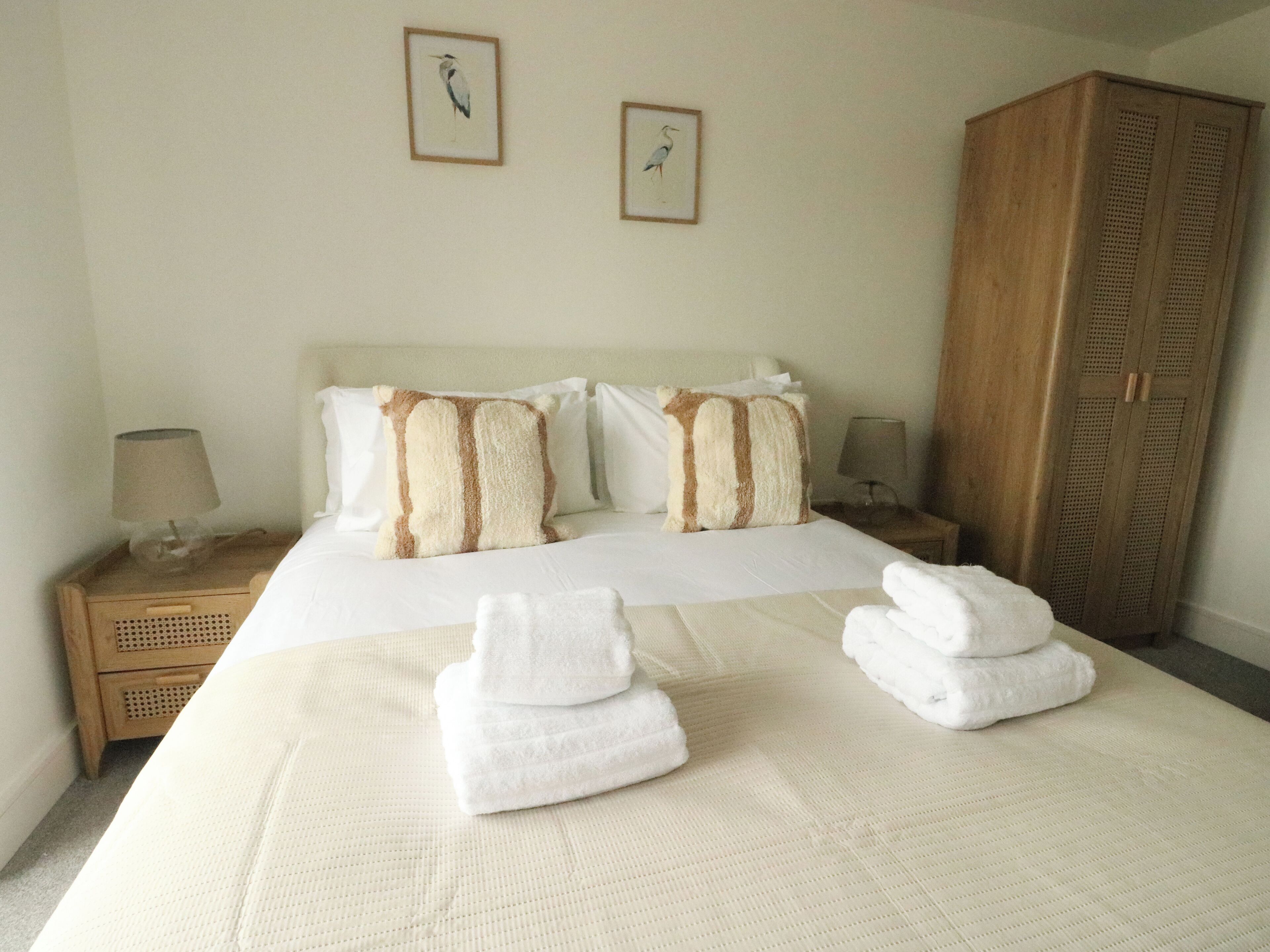 A hotel room with a neatly made bed, two pillows, a wooden wardrobe, and two framed pictures on the wall.