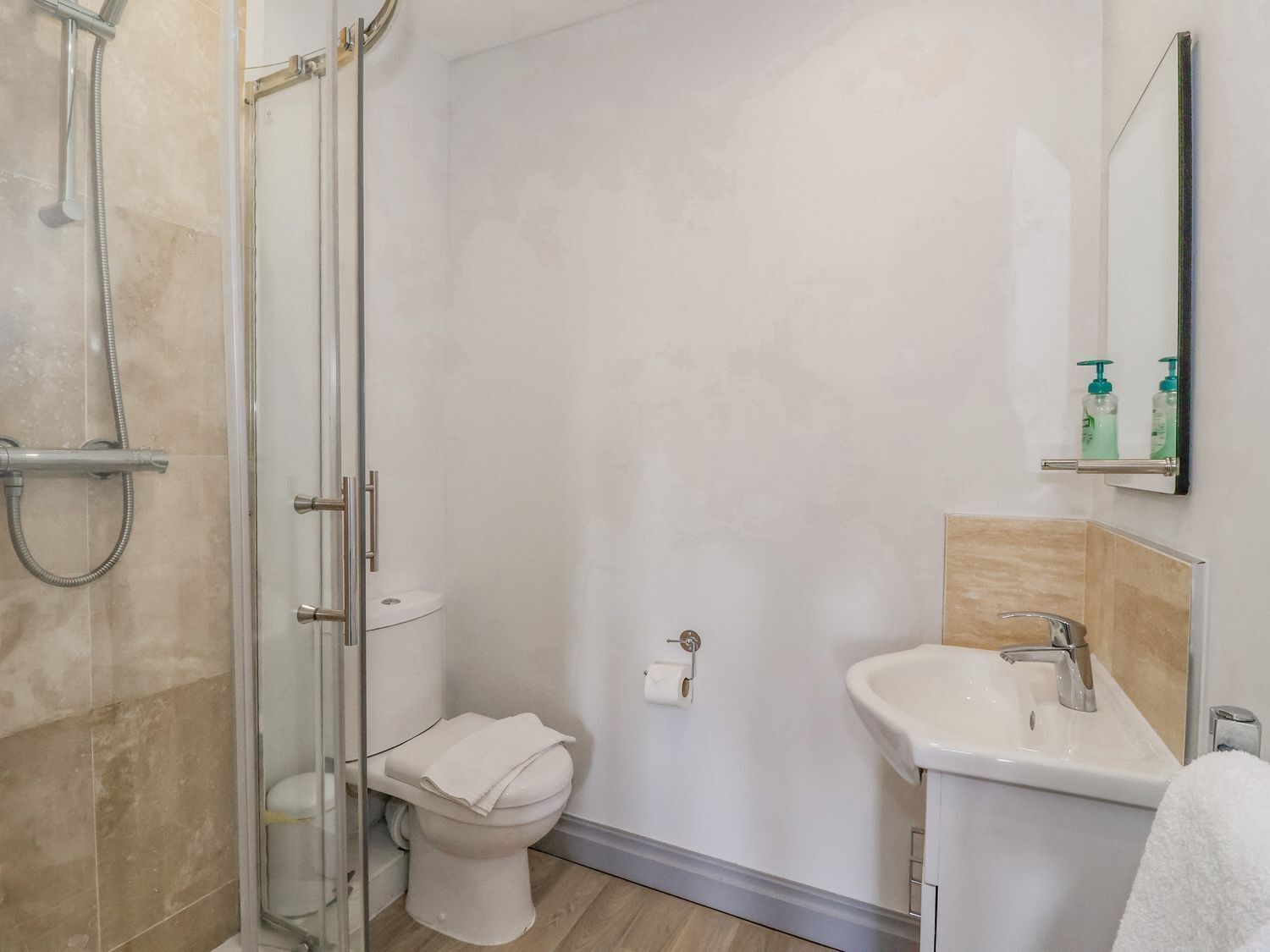 Un baño con ducha de vidrio, inodoro y lavamanos con espejo.