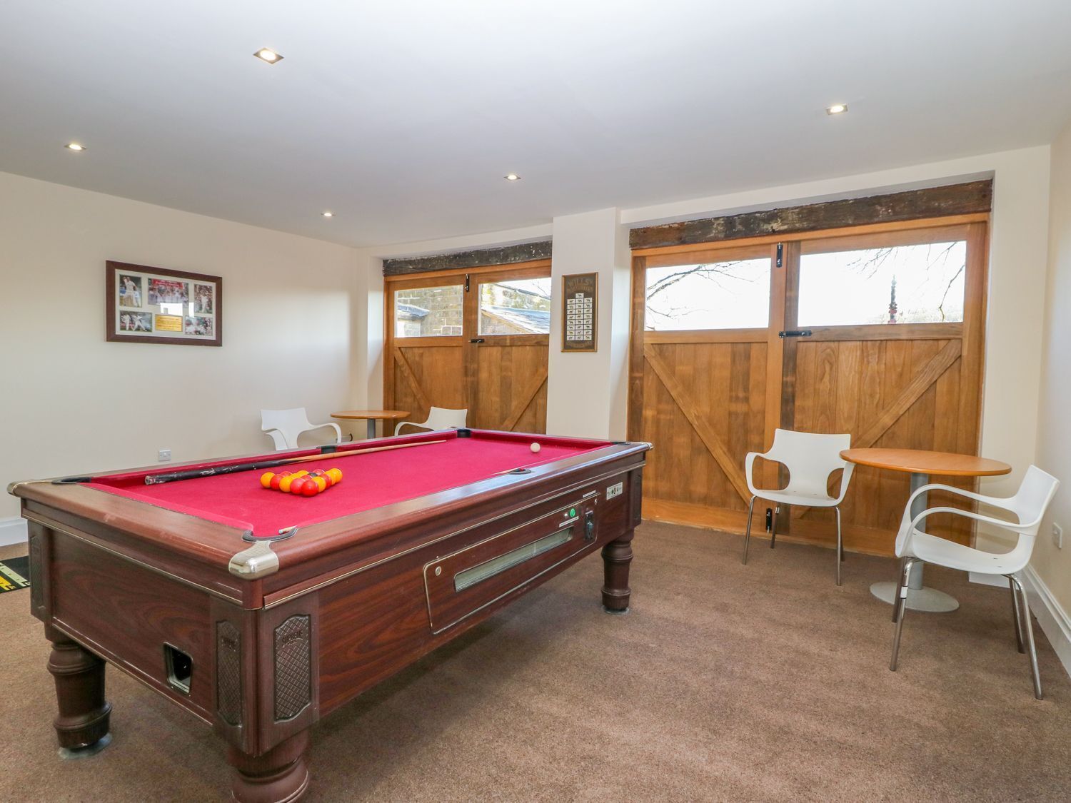 A pool table with a red felt surface, surrounded by white chairs and a small table.