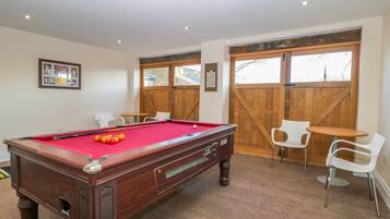 A pool table with a red felt surface, surrounded by white chairs and a small table.