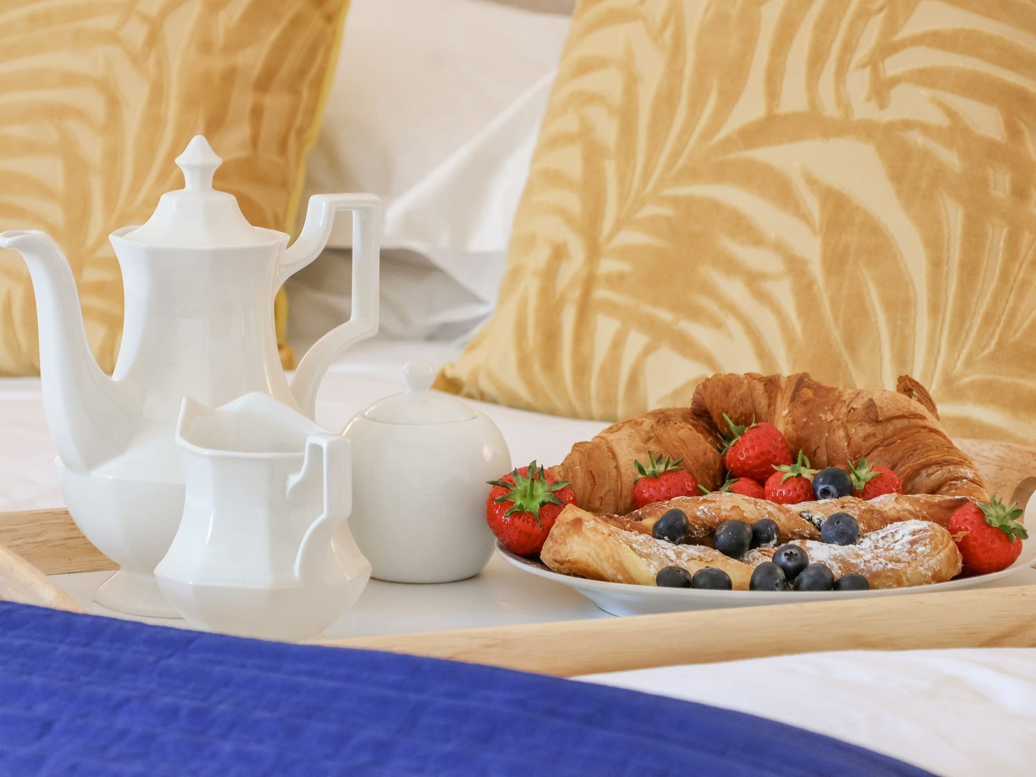 A breakfast setup with a teapot, cups, and a plate of croissants with strawberries and blueberries.