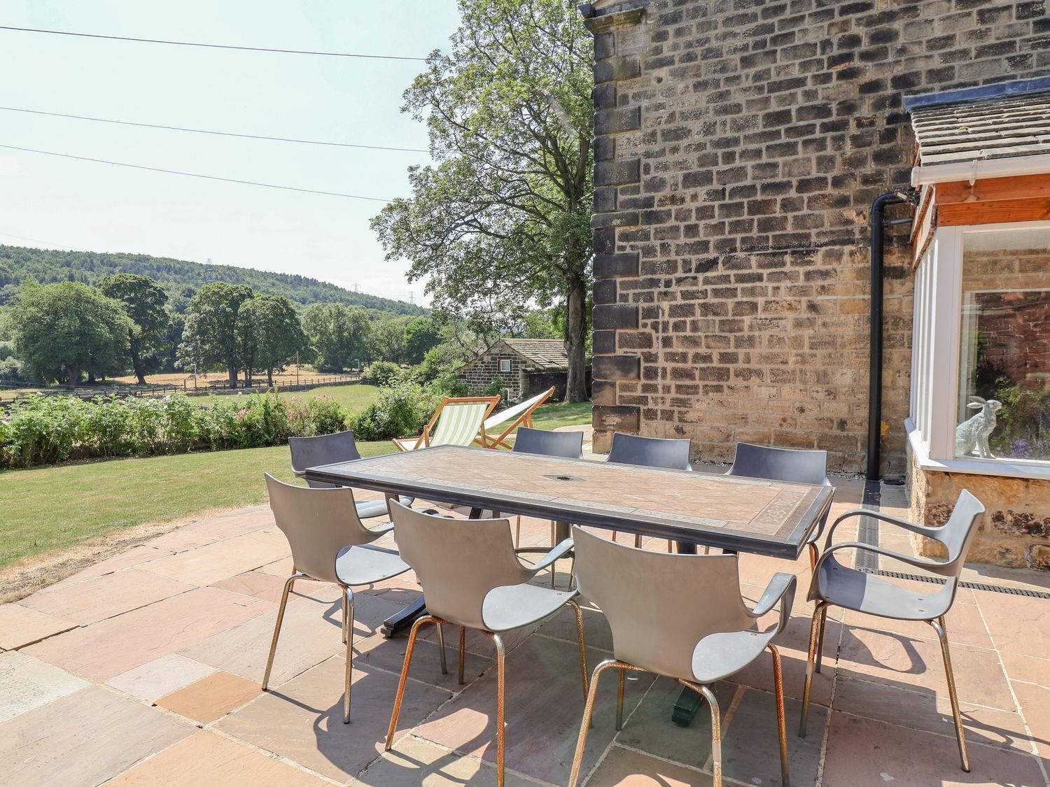 Une terrasse avec une table et des chaises, un mur en pierre et une vue sur un paysage verdoyant.