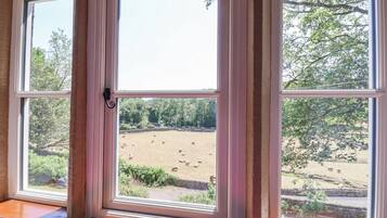 Een kamer met een groot raam dat uitkijkt op een omheind buitengebied met schapen.