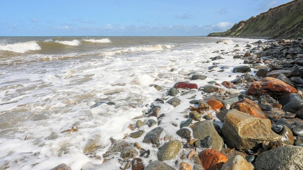 Ein felsiger Strand mit brechenden Wellen und einer Klippe im Hintergrund.