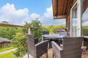 A wooden deck with wicker furniture and a glass door leading to a lush green landscape. - 3 Lake View (Looe)