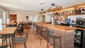 Una zona de bar con suelo de madera, taburetes, una barra con dispensador de bebidas y estantes llenos de botellas.
